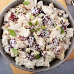 Chicken salad with dried cherries, almonds, and fresh greens in a white bowl