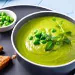 Bowl of creamy green pea soup garnished with fresh mint