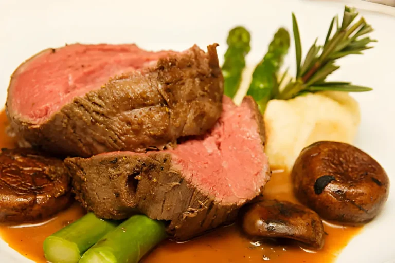 Sliced prime rib arranged on a serving platter, surrounded by roasted asparagus spears and golden brown mushrooms. Fresh herbs garnish the dish.